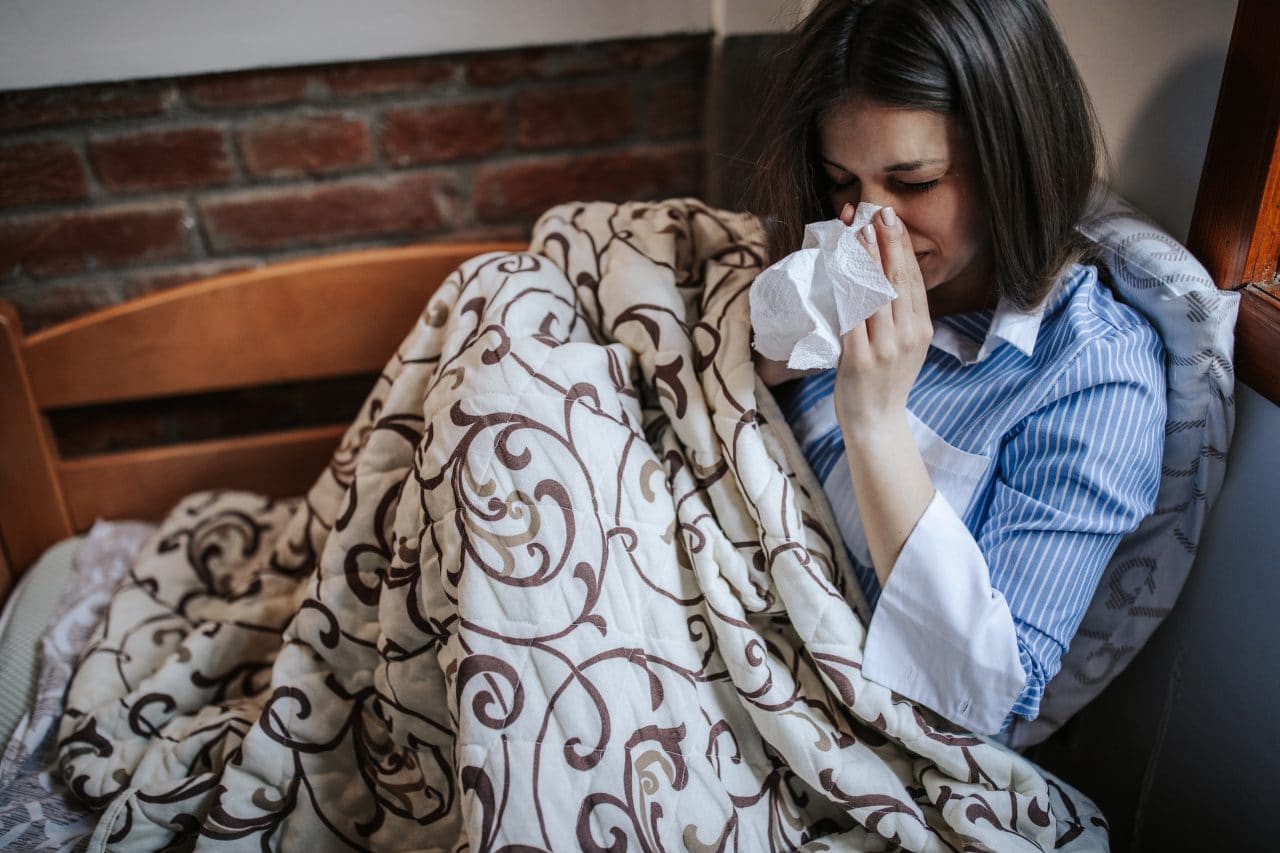 Young sick woman with allergies, sitting in bed and blowing nose