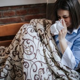 Young sick woman with allergies, sitting in bed and blowing nose