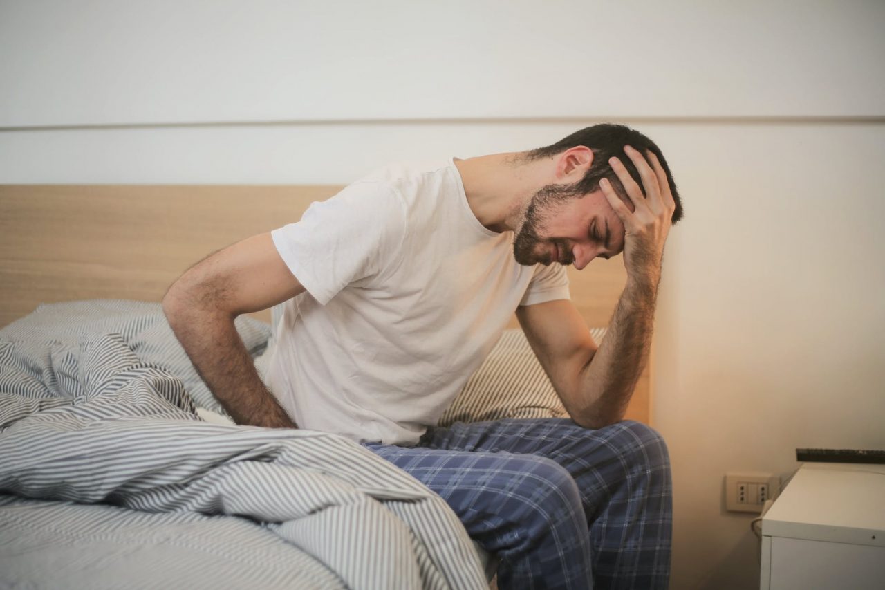 Man with a headache sitting on the edge of his bed.