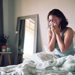 Woman blowing her nose while in bed.