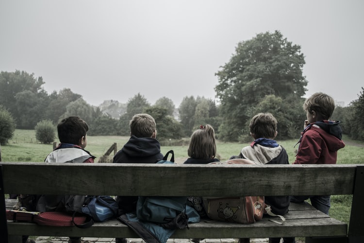 A group of children gathering on a bench outside.