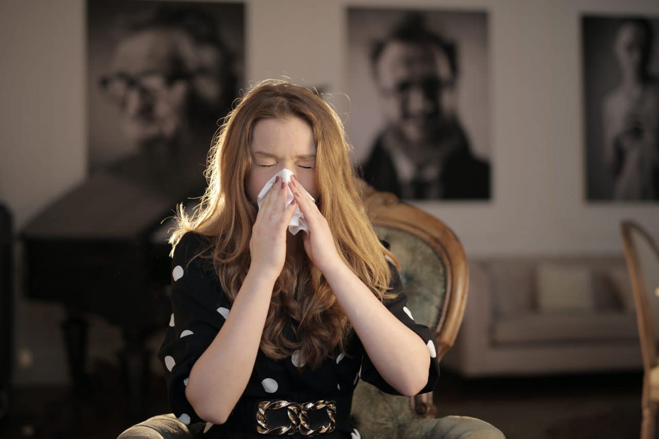 A woman using a tissue to cover her sneeze.