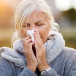 Older woman with allergies blowing her nose.