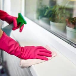 Person wiping off their window sill with spray cleaner.