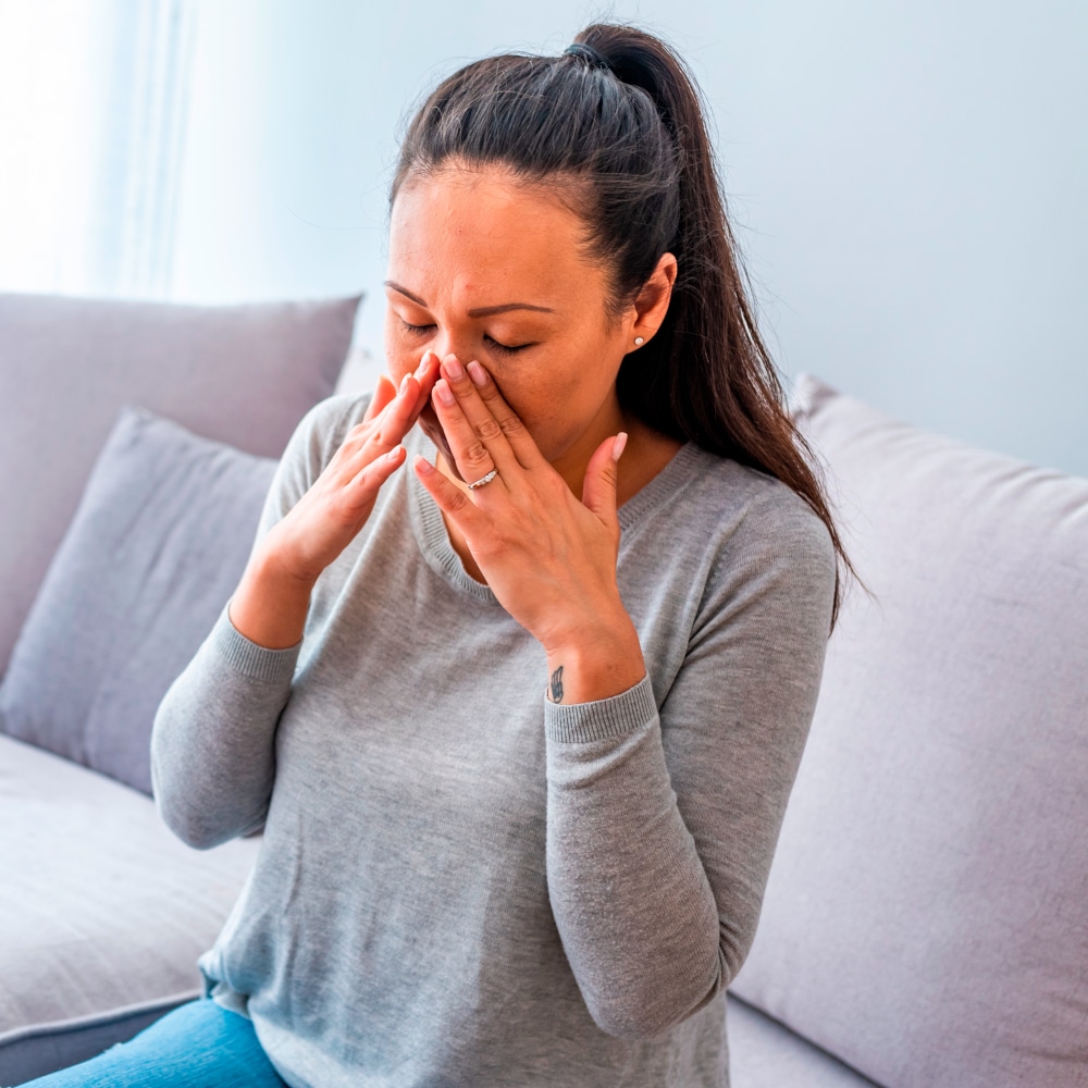 a woman presses on her nose to relieve sinus pressure, a common symptom of allergies