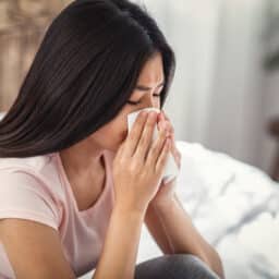 Woman in bed with allergies blowing her nose.