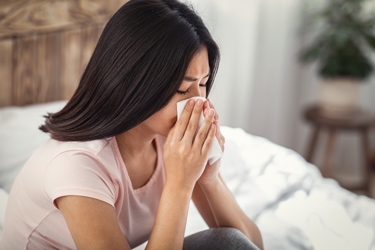 Woman in bed with allergies blowing her nose.