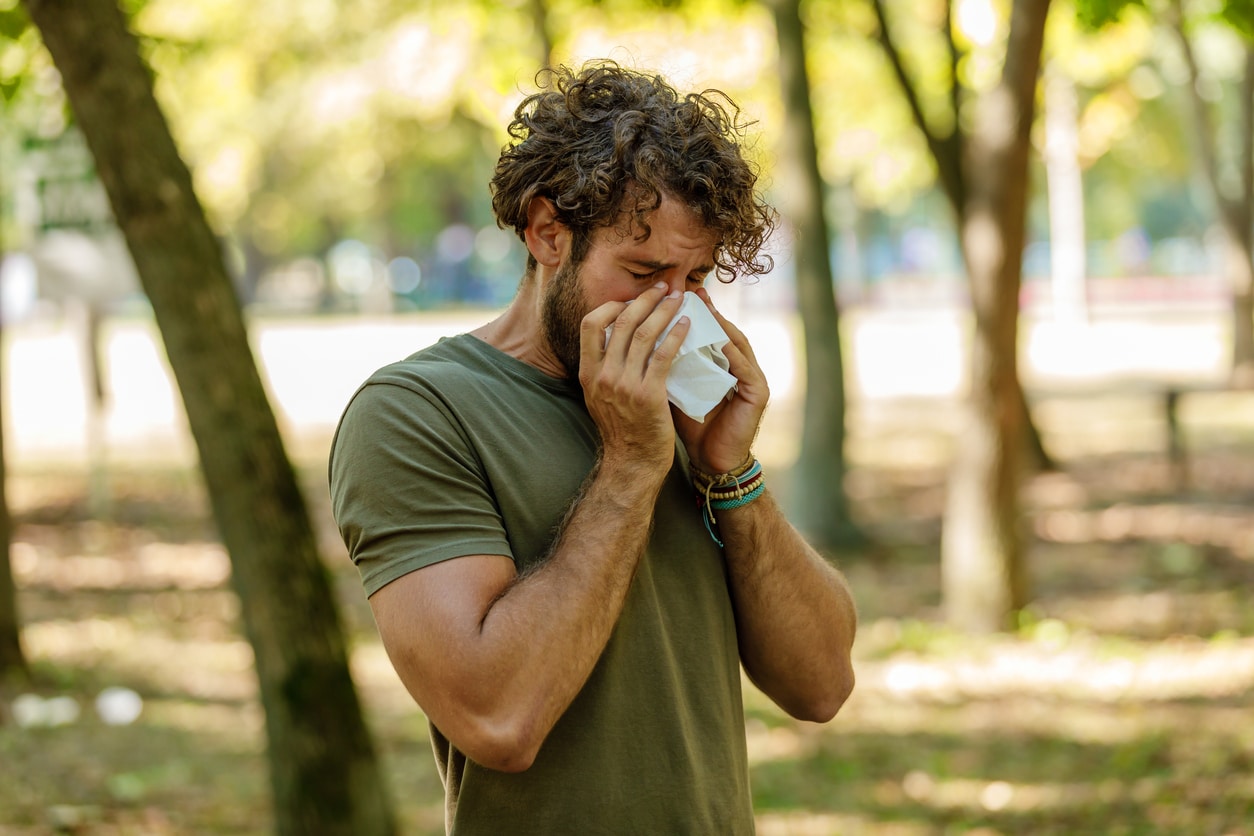 Man sneezing into a tissue at the park.