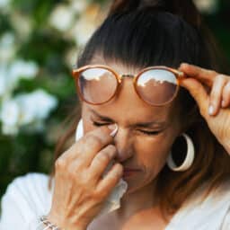 Woman with allergies rubbing her eye with a tissue