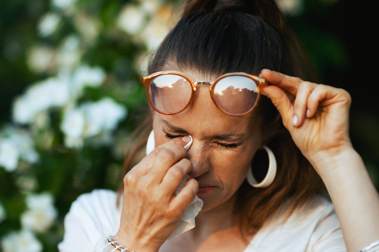 Woman with allergies rubbing her eye with a tissue.