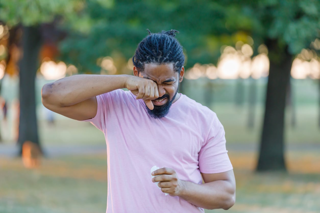 Man with allergies scratches eyes in park