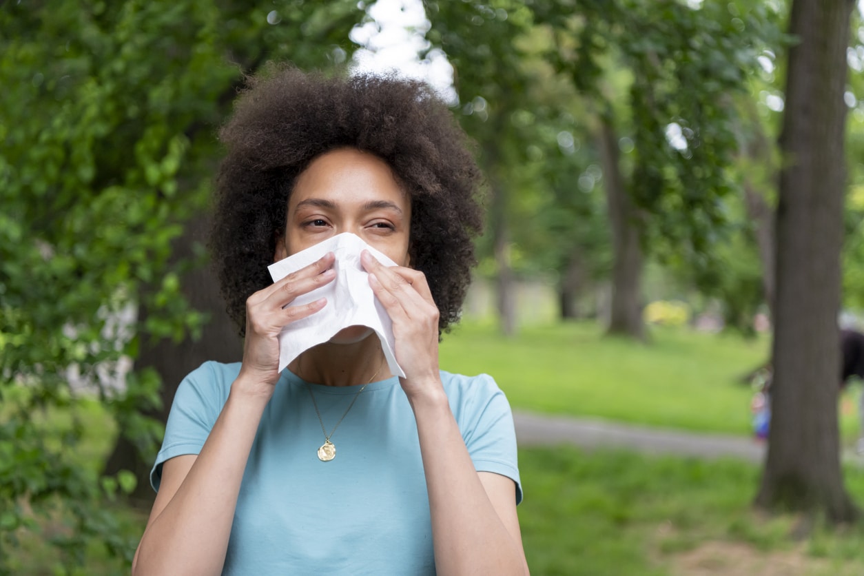 Woman with environmental allergies sneezing into a tissue.